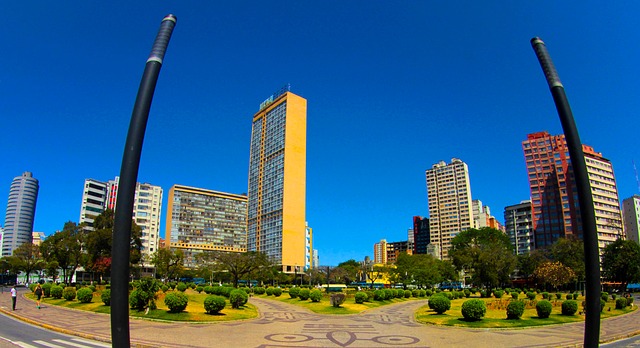 Praça Raul Soares, com grama e jardins em tons de verde,  com edifício de paredes amarelas, prédios ao redor e céu azul de inverno no Brasil